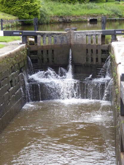 A lock gate slowly letting out water to lower a narrow boat to the stretch below.